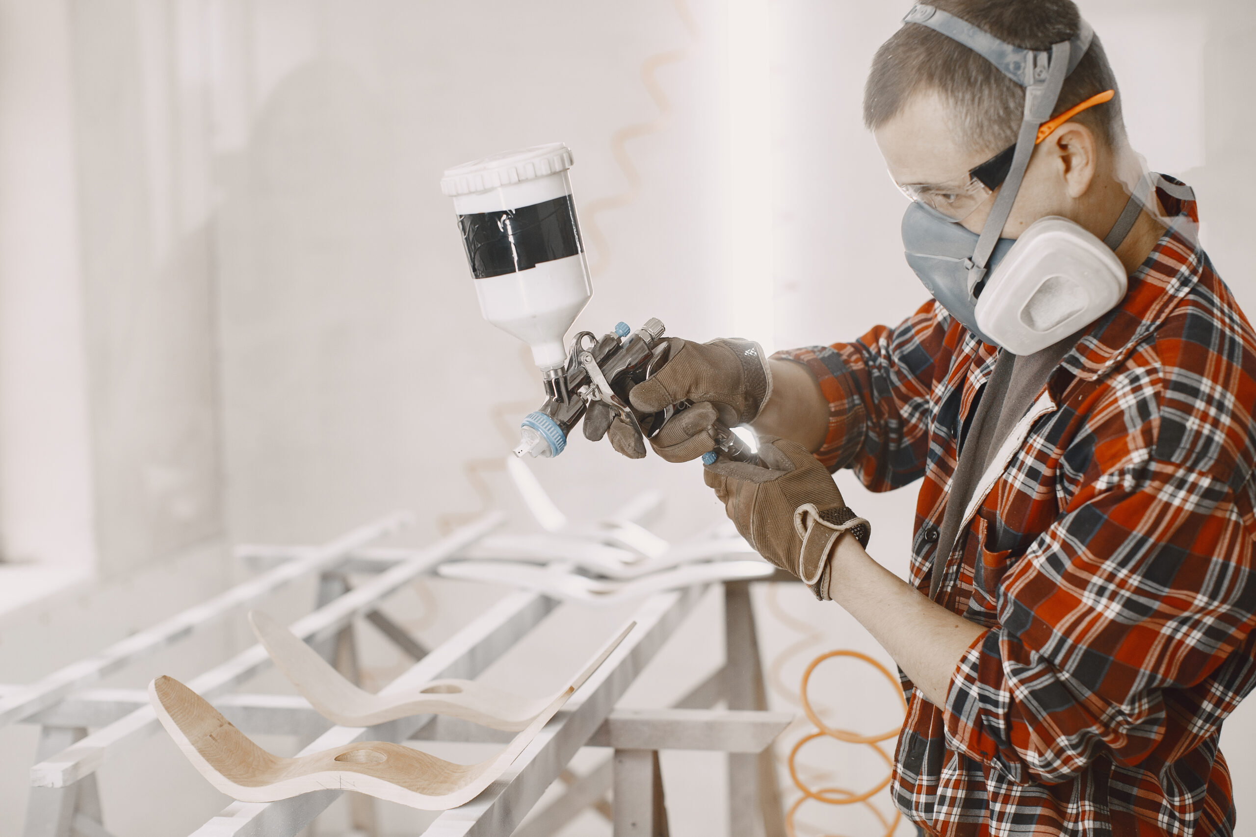 Professional technician in a full-face respirator applying a precision spray painting to a curved plastic component with fine-detail features.